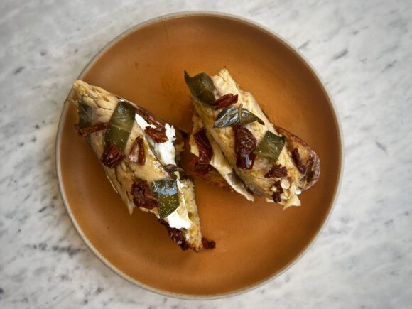 Sourdough toast topped with Sicilian mackerel fillets, sun-dried tomatoes, and caper leaves in olive oil.